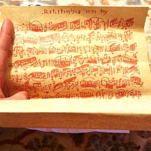 May include: A rectangular piece of aged, tan parchment paper featuring hand-drawn musical notation in bright red ink. The top section displays the text Rsthtnhia in by, followed by several staves of complex, dense musical notes and symbols.
