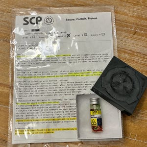May include: A clear plastic bag containing a white document with SCP Foundation text and a logo, a small glass vial with a yellow label marked SCP-008, and a black square object with a circular embossed design on its top surface.