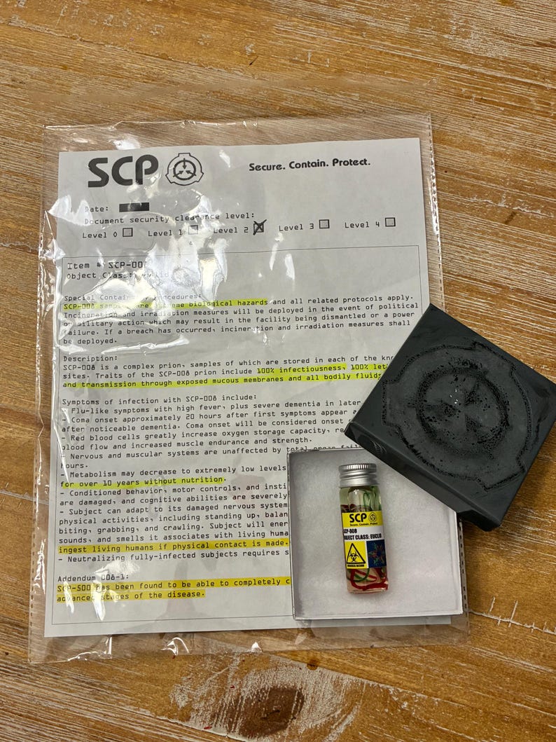 May include: A clear plastic bag containing a white document with SCP Foundation text and a logo, a small glass vial with a yellow label marked SCP-008, and a black square object with a circular embossed design on its top surface.