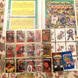 May include: A collection of Garbage Pail Kids trading cards and related items, including a binder, packs, and individual cards. The cards feature colorful, cartoonish illustrations of grotesque characters. The binder has a green spine and the cover reads "Garbage Pail Kids Flashback."