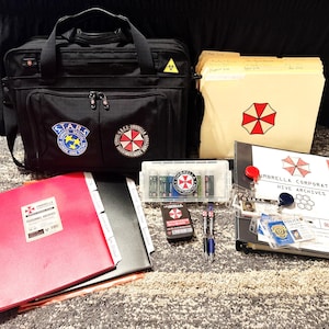 May include: A black tactical bag with S.T.A.R.S. and Umbrella Corporation patches, a beige file folder with a red and white umbrella logo, a black binder labeled Umbrella Corporation Hive Archives, a red folder, a clear case, and ID badges.