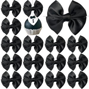 May include: A collection of black satin bows arranged in a grid, featuring a single round cake pop decorated to resemble a tuxedo with a white shirt front, black lapels, and two small black buttons, all set against a plain white background.