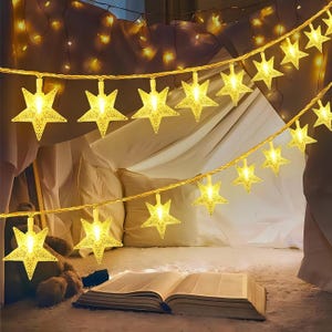 May include: A string of LED fairy lights featuring multiple five-pointed star-shaped covers with a textured, translucent finish. Each star emits a warm yellow glow, connected by a thin, flexible wire that is draped across the space.