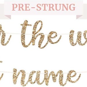 May include: A gold glitter banner with the phrases "pour the wine" and "his last name is mine" in cursive script. The banner is pre-strung and ideal for a wedding or bachelorette party. A pink banner above reads "PRE-STRUNG".