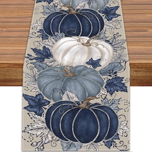 May include: A table runner featuring a repeating pattern of pumpkins in shades of navy blue, light blue, and white. The design includes detailed illustrations of dark blue and white autumn leaves, vines, and stems on a light beige background.
