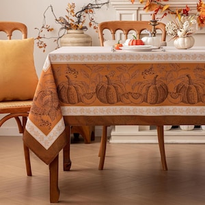 May include: A rectangular tablecloth featuring a warm orange background with a repeating pattern of pumpkins, autumn leaves, and turkeys. The design includes a decorative border of white leaves on a light background, creating a seasonal aesthetic.