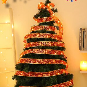 May include: A dark green artificial Christmas tree decorated with a long, shimmering red ribbon featuring a gold star pattern. The ribbon is wrapped spirally around the tree and is illuminated by small, integrated warm white LED string lights.