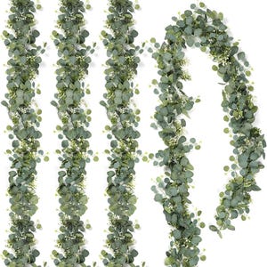 May include: A set of four artificial garlands featuring realistic green eucalyptus leaves and small white flower clusters. Three of the garlands are displayed in straight vertical lines, while the fourth is arranged in a curved, draped shape.