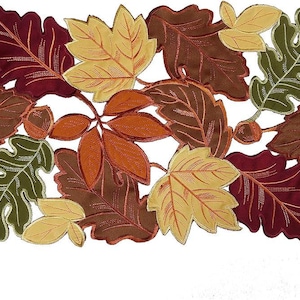 May include: A rectangular table runner featuring a dense, overlapping pattern of autumn leaves in shades of deep red, burnt orange, golden yellow, and forest green, interspersed with small brown acorns throughout the entire design.