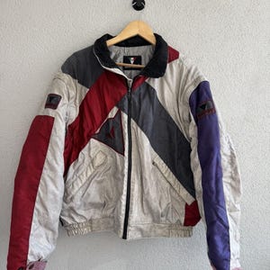 以下が含まれることがあります： 黒い持ち手と「But First, Coffee」の太字の黒い文字が入った白いセラミックマグカップ。マグカップはぼやけた背景に置かれており、居心地の良い環境を示唆しています。