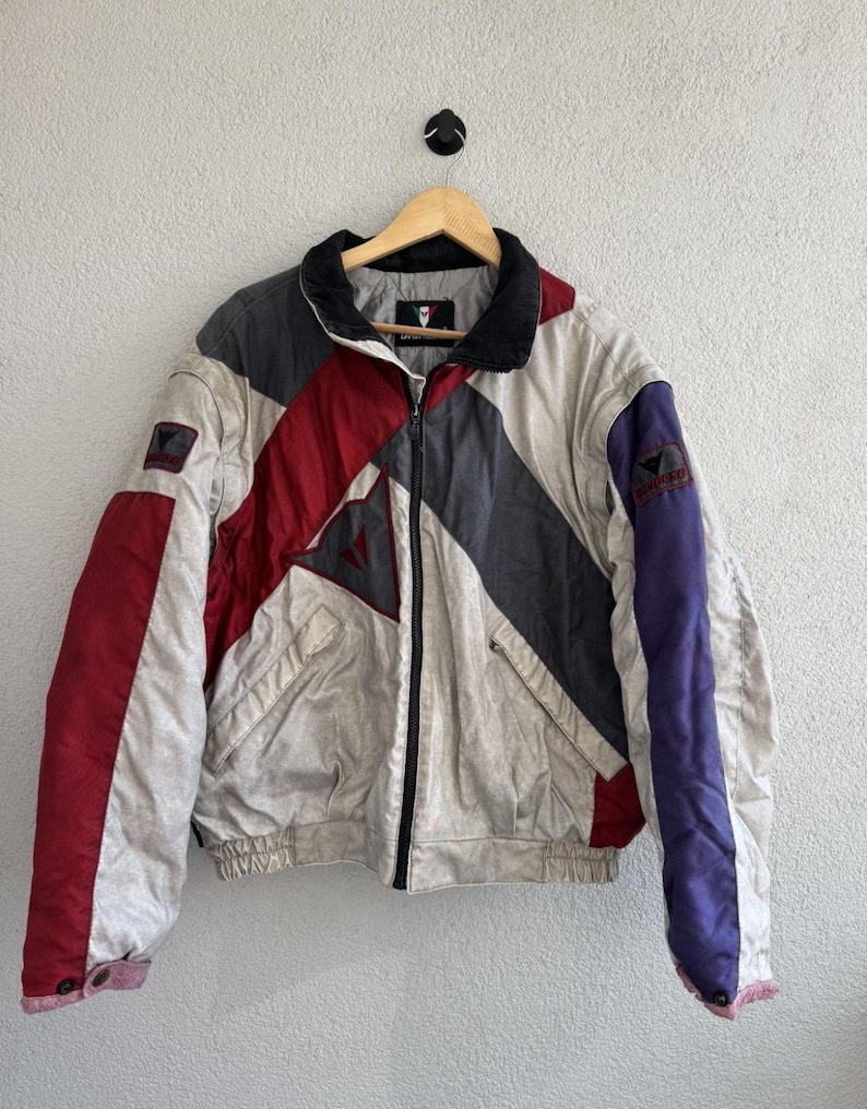 以下が含まれることがあります： 黒い持ち手と「But First, Coffee」の太字の黒い文字が入った白いセラミックマグカップ。マグカップはぼやけた背景に置かれており、居心地の良い環境を示唆しています。