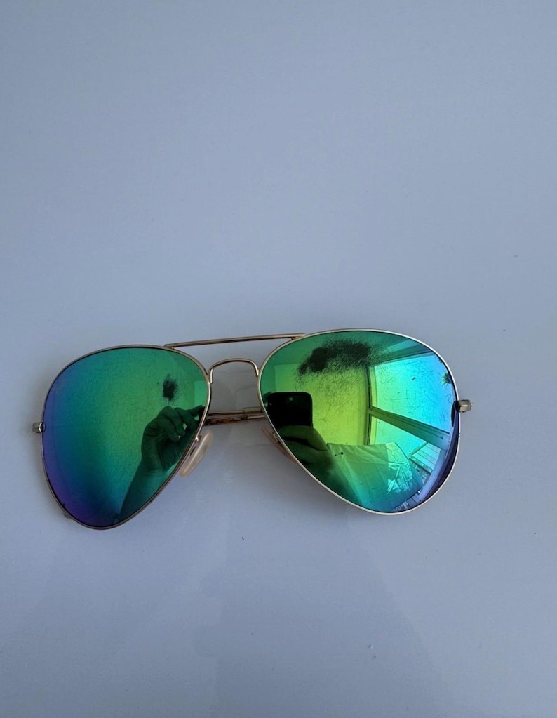 K&ouml;nnte beinhalten: Aviator-Sonnenbrille mit goldfarbenem Gestell und gr&uuml;n verspiegelten Gl&auml;sern. Die Gl&auml;ser spiegeln die Umgebung wider. Die Sonnenbrille hat eine klassische Tropfenform und einen Doppelsteg.
