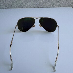K&ouml;nnte beinhalten: Sonnenbrille im Aviator-Stil mit einem goldfarbenen Metallrahmen und dunkelgr&uuml;nen Gl&auml;sern. Die Sonnenbrille hat einen Doppelsteg und gebogene B&uuml;gel. Die Gl&auml;ser sind tropfenf&ouml;rmig.