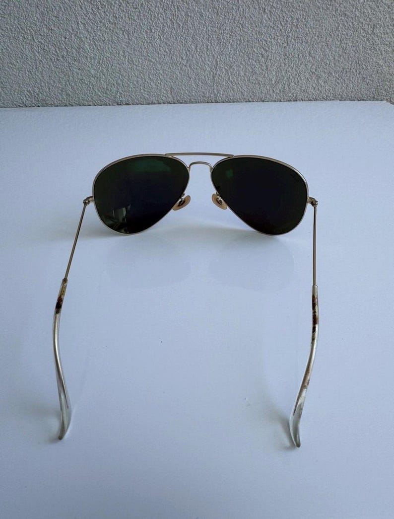 K&ouml;nnte beinhalten: Sonnenbrille im Aviator-Stil mit einem goldfarbenen Metallrahmen und dunkelgr&uuml;nen Gl&auml;sern. Die Sonnenbrille hat einen Doppelsteg und gebogene B&uuml;gel. Die Gl&auml;ser sind tropfenf&ouml;rmig.