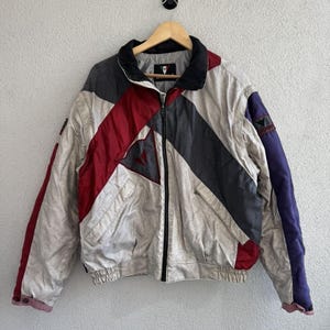 以下が含まれることがあります： クリーム、赤、グレー、ネイビーブルーのヴィンテージカラーブロックジャケット。 ジャケットは黒い襟、フルレングスのジッパー、胸にロゴが付いています。 ジャケットはリブ編みの裾と袖口が付いています。 ジャケットは木製のハンガーに掛かっています。