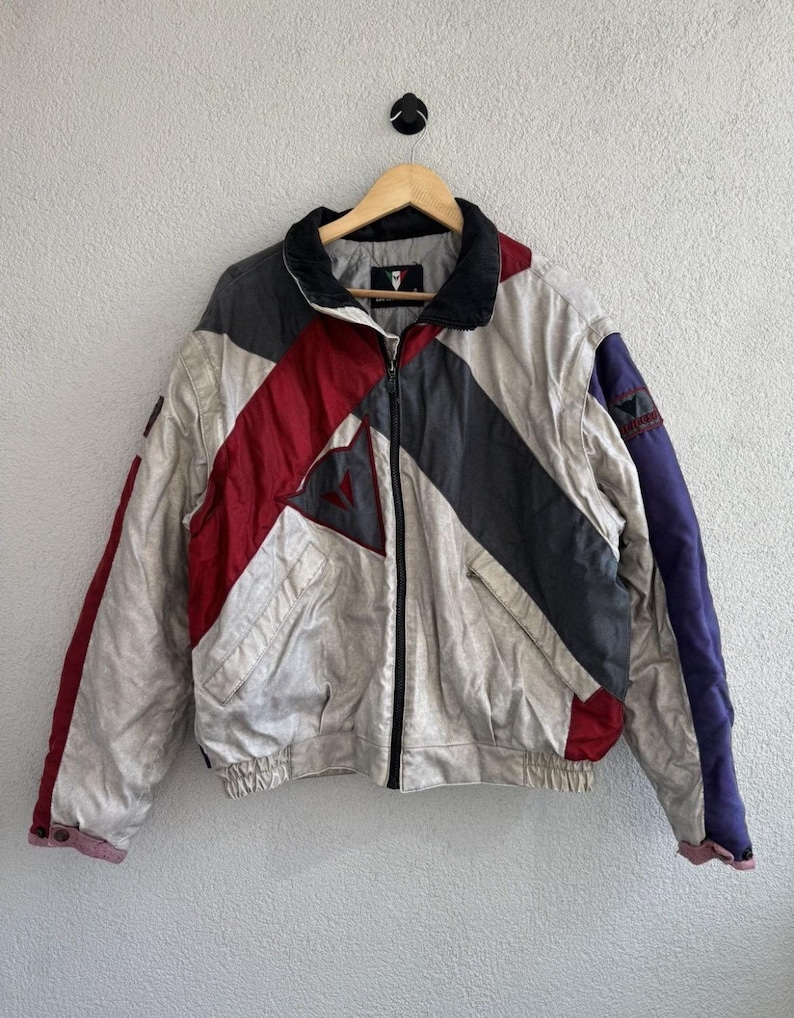 以下が含まれることがあります： クリーム、赤、グレー、ネイビーブルーのヴィンテージカラーブロックジャケット。 ジャケットは黒い襟、フルレングスのジッパー、胸にロゴが付いています。 ジャケットはリブ編みの裾と袖口が付いています。 ジャケットは木製のハンガーに掛かっています。