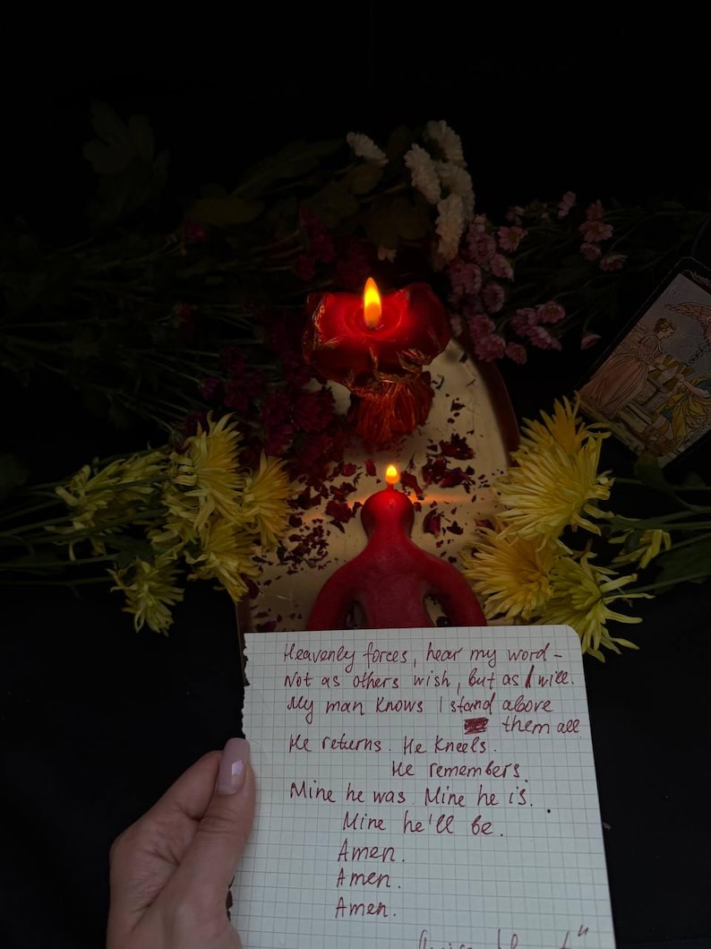May include: A red candle with a flame, shaped like a person, is lit. A handwritten note with text is held in front of the candle. Yellow and pink flowers are in the background.