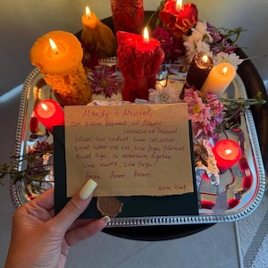 A hand holding a handwritten note with a warm, intimate message, surrounded by a tray of lit candles and flowers, creating a cozy and romantic atmosphere.