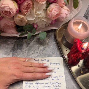 A bouquet of pink and white roses, a candle, and a handwritten note on a gray marble surface.
