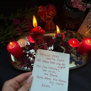 Puede incluir: Un arreglo con velas rojas encendidas, p&eacute;talos secos y una nota manuscrita. La nota dice "Celestial forces...Aviva Hart spells." La escena est&aacute; dispuesta sobre una bandeja plateada con un fondo oscuro.