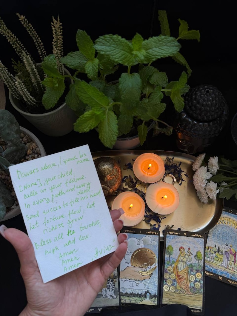 May include: A spiritual scene featuring lit candles, tarot cards, and fresh mint plants. A handwritten note with text is held in the foreground. The scene is set on a gold tray with a dark background.