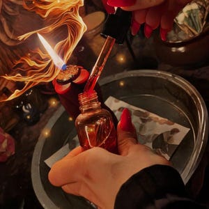 Puede incluir: Una peque&ntilde;a botella de vidrio color &aacute;mbar con un cuentagotas es sostenida por una persona. El cuentagotas dispensa un l&iacute;quido rojo. Una vela encendida y una ilustraci&oacute;n decorativa est&aacute;n en el fondo.