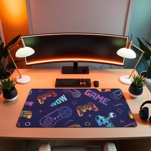 May include: A gaming desk setup featuring a curved monitor, keyboard, mouse, and a large mousepad. The mousepad is navy blue with colorful game controller graphics and the words "WOW" and "GAME". Two desk lamps and potted plants flank the monitor.