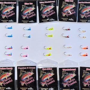 May include: A selection of Fishin Freekz fishing lures in diverse colours, such as blue, yellow, pink, and orange. Each lure is attached to a small hook. The packaging displays the brand name and product details.