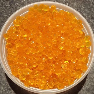 May include: A white plastic bowl filled with bright orange, translucent spheres. The spheres are densely packed, creating a textured surface. The image is a close-up, highlighting the color and texture of the food.