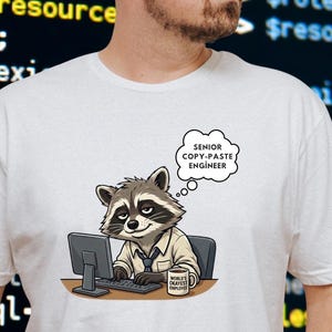 May include: White t-shirt featuring a cartoon raccoon wearing a shirt and tie, sitting at a computer. A thought bubble above the raccoon reads "SENIOR COPY-PASTE ENGINEER." A coffee mug on the desk says "World's Best Employee."