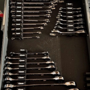 Puede incluir: Una colección de llaves de metal de color plateado organizadas en un cajón de herramientas. El juego incluye varios tamaños que van desde 7 mm hasta 19 mm, con cada llave sujeta por un organizador de plástico negro etiquetado con su tamaño métrico.