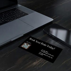 May include: A laptop, smartphone, and business card are arranged on a dark, textured surface. The business card, with the text "Book Your Ride Today!", includes a QR code and contact information. The smartphone is black and sleek.