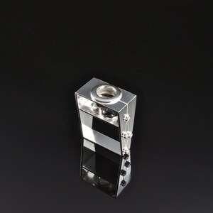 May include: A silver ring with a square design and a circular opening in the center. The ring has a small green stone and silver beads on the side.