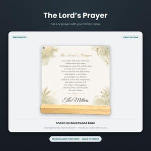 May include: A square plexiglass print featuring The Lord's Prayer in black text with gold accents, decorated with botanical illustrations in the corners. The print is displayed on a light-colored rectangular beechwood base.
