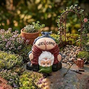 Può includere: Una statua di gnomo da giardino stravagante in posa piegata, che rivela la parola "WELCOME" sulla schiena. Lo gnomo indossa una giacca rossa, un cappello blu e scarpe nere. Un piccolo uccello blu è appollaiato sul cappello dello gnomo. La scena include una piccola succulenta.