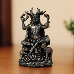 May include: A detailed figurine of Cernunnos, a horned deity, in a seated pose. The statue is primarily silver and black, with intricate detailing on the figure's face, antlers, and clothing. Two small animals flank the base of the statue.