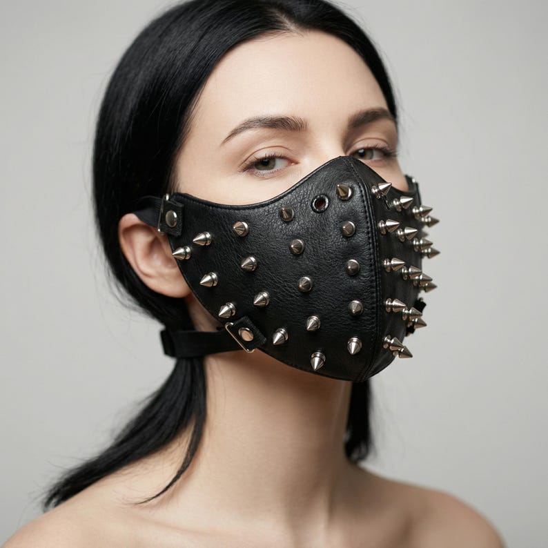 May include: Black leather face mask with silver metal spikes. The mask covers the nose and mouth, secured with adjustable straps. The mask has a punk rock or alternative aesthetic.
