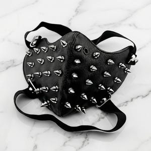 May include: Black leather face mask with numerous silver-colored cone studs. The mask has black straps and metal hardware for attachment. The mask is designed to cover the nose and mouth.