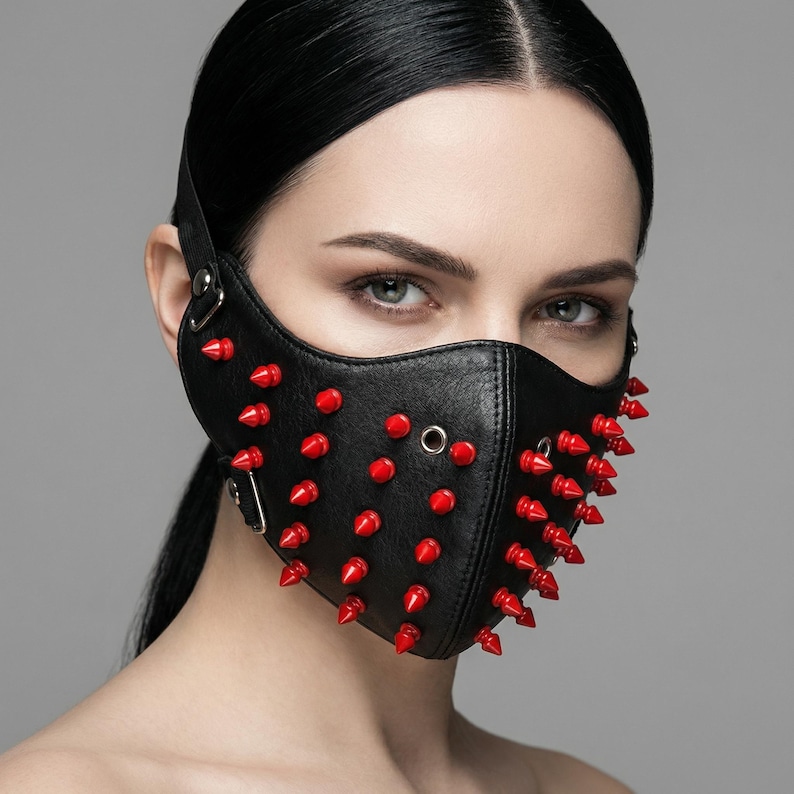 May include: Black leather mask with red spikes. The mask covers the nose and mouth, secured with a strap around the head. The mask has metal eyelets and a buckle. The spikes are evenly spaced across the mask's surface.