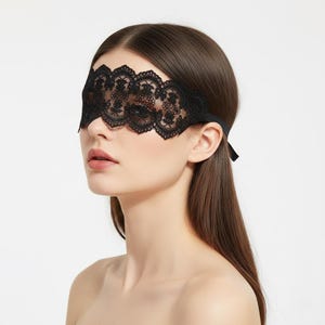 May include: Black lace eye mask with a floral design. The mask covers the eyes and is secured with a thin black strap tied at the back of the head. The mask is made of delicate, intricate lace.