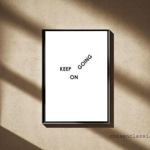 Puede incluir: Impresión blanca enmarcada con las palabras "KEEP ON GOING" en fuente negra. La impresión está colocada contra una pared beige con sombras. La dirección del sitio web chosenclassics.com está en la esquina inferior derecha.