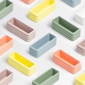 Puede incluir: Una colecci&oacute;n de bandejas de almacenamiento rectangulares dispuestas en un patr&oacute;n de cuadr&iacute;cula. Cada bandeja presenta un dise&ntilde;o de pared exterior acanalado de varias capas y viene en varios colores pastel, incluyendo verde salvia, amarillo p&aacute;lido, rosa suave, blanco y azul claro.