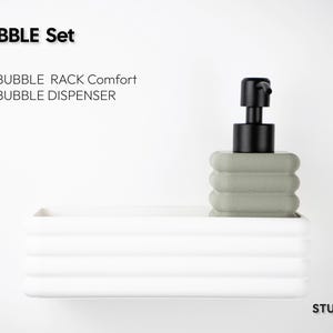 Puede incluir: Un conjunto BUBBLE que incluye un estante rectangular blanco con crestas horizontales y un dispensador de jab&oacute;n cuadrado de color verde salvia con una bomba negra. El texto BUBBLE Set, BUBBLE RACK Comfort + BUBBLE DISPENSER y STUDIO 23 es visible.