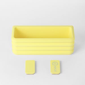Puede incluir: Un recipiente rectangular amarillo con un dise&ntilde;o exterior acanalado. Debajo del recipiente hay dos peque&ntilde;os accesorios rectangulares amarillos, uno de los cuales tiene el texto "STUDIO 23" impreso en color gris claro en su superficie.