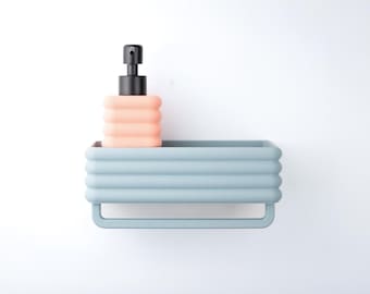 Puede incluir: Un estante de pared rectangular de color azul claro con un exterior texturizado y acanalado, que incluye una barra para toallas integrada y sostiene un dispensador de jabón color melocotón con bomba negra.