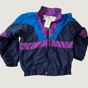 May include: A color-blocked windbreaker jacket featuring a high collar, a full-length front zipper, and elasticized cuffs and hem. The design incorporates panels of navy blue, bright blue, and purple, with a white brand tag attached to the zipper.