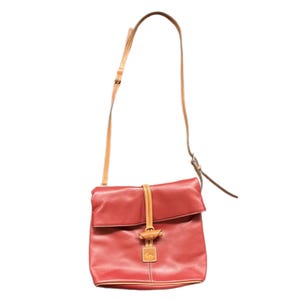 May include: Red leather crossbody bag with a tan leather strap and accents. The bag has a flap closure with a tan leather strap and a small logo tag. The bag is approximately 10 inches wide and 10 inches tall.