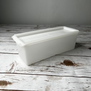 May include: A rectangular white plastic storage container with a matching fitted lid. The container features a smooth, opaque finish and a clean, simple design with slightly tapered sides, providing a functional solution for organizing household items.