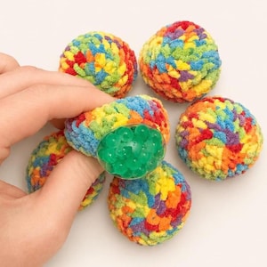 May include: A collection of colorful, rainbow-hued stress balls. One ball is being held, revealing a clear, circular section filled with green gel beads. The balls are made of a soft, textured material, with a variety of colors.