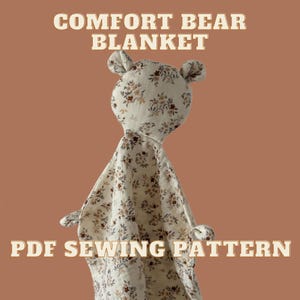 Op de afbeelding: Een crèmekleurig stoffen knuffeldoekje in de vorm van een berenkop met kleine oortjes en armpjes, voorzien van een bruin en beige bloemenpatroon. De tekst COMFORT BEAR BLANKET en PDF SEWING PATTERN staat in wit met een bruine omlijning.